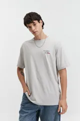 Remera de manga corta color gris claro, con cuello redondo y estampado pequeño en el pecho con texto en rojo y negro.