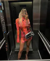 Vestido corto de microtul elastizado con estampado floral en tonos naranja, rosa y negro. Tiene cuello alto y mangas largas acampanadas.