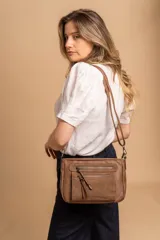 Bandolera de simil cuero color marrón topo, con textura ligeramente desgastada y detalles en nobuck. Presenta múltiples bolsillos frontales con cierres metálicos y tiradores de cuero. Correa ajustable para llevar al hombro o cruzada.