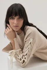 Sweater beige de tejido de punto con cuello redondo y mangas largas con detalle de cordones cruzados en los brazos.