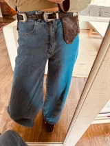 Cinturón ancho de cuero marrón oscuro con borde festoneado y cordones cruzados en la parte superior.