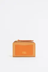 Monedero negro de piel con estructura rígida, logo metálico dorado, tirador de cordón y acabados metálicos dorados. Tarjetero interior, cierre con botón de presión e interior con logo grabado. Confeccionada en 100% poliéster reciclado y 100% poliuretano de producción responsable.