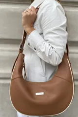 Cartera tipo hobo de cuero color marrón con correa de hombro ajustable y cierre superior. Tiene un bolsillo interno con cierre y un bolsillo trasero externo con cierre.