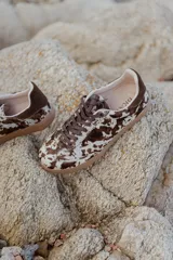 Zapatilla urbana con capellada de cuero con textura tipo pelo con estampado animal print en marrón y blanco, detalles en gamuza marrón, cordones marrones y suela de goma color caramelo.