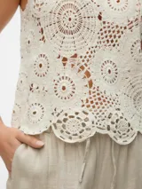 Top sin mangas color blanco roto, tejido a crochet con motivos circulares y borde festoneado.