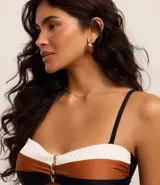 Top de bikini bandeau con bloques de color blanco, marrón y negro. Tiene breteles ajustables y removibles, relleno removible, adorno metálico en el centro del busto y lazo en la espalda.