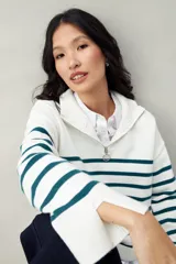 Polera blanca de punto con cuello alto y cierre metálico, de calce relajado y diseño a rayas horizontales azules.