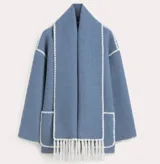 Conjunto de saco y bufanda color gris oscuro con detalles de costura en blanco. El saco es de corte holgado, con cuello alto, cierre frontal con botones, bolsillos frontales y mangas largas. La bufanda es larga y con flecos.