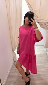 Vestido corto color fucsia, de lino, con cuello redondo y mangas cortas. Es más corto adelante que atrás, con corte transversal en la falda.