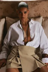 Falda pantalón color beige, de tiro alto, con bolsillos laterales tipo cargo, detalle de tablas y cierre lateral con cremallera oculta y trabilla con hebilla metálica.