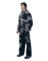 Pantalón unisex de denim 100% algodón con lavado overo (manchas grises sobre negro). Calce wide/relajado, tiro medio, pierna extra ancha y caída larga. Cintura con elásticos laterales, costuras curvas, bolsillos delanteros y traseros curvos, presillas para cinto, cierre y botón metálico.