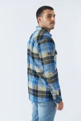 Sobrecamisa de algodón para hombre con interior de corderito, estampado a cuadros en tonos negro, blanco y azul. Tiene cierre de botones, bolsillos tipo cartera y logo en goma. El modelo usa talle M.
