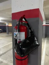 Cartera negra charolada con asa corta y cierre de cremallera. Tiene un aplique metálico en forma de estrella.