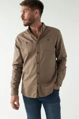 Camisa de hombre color marrón con efecto stone wash, fit regular, cuello americano, cierre con botones, dos bolsillos frontales con botón y mangas largas con puños abotonados.