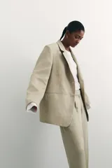 Blazer color beige de corte holgado con solapas de muesca, hombreras, abertura y botón en los puños, bolsillos delanteros ribeteados y bolsillo superior ribeteado. Forrado.