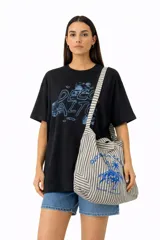 Bolso tipo shopper de lona con estampado a rayas verticales en tonos beige y gris oscuro. Presenta un estampado frontal en azul que incluye una figura ecuestre bajo una palmera.