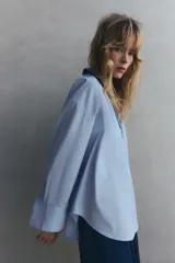 Camisa celeste de popelina de algodón, con cuello solapa, escote pico, manga larga con puños y cierre frontal con botones.