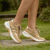 Zapatillas deportivas color beige con detalles dorados, cordones al tono y suela blanca.