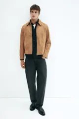 Campera de gamuza color camel, con cuello camisero, cierre frontal y bolsillos laterales con cierre. Presenta un corte estándar y forro interior.