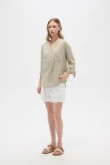 Blusa color beige con estampado de arabescos blancos, cuello mao, mangas 3/4 con lazos en los puños, cierre parcial con botones y bolsillos frontales.