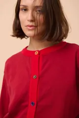 Cárdigan negro de punto con cuello redondo, cierre frontal con botones celestes y ribetes en cuello y puños de color rojo.