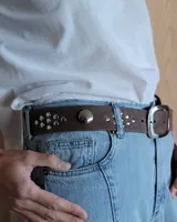 Cinto marrón de cuero con tachas plateadas y doradas, y hebilla metálica rectangular color bronce.