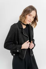 Chaqueta negra tipo biker de gamuza sintética con cuello solapa y manga larga con trabillas en los hombros. Tiene bolsillos delanteros con cremallera metálica y cierre frontal con cremallera.