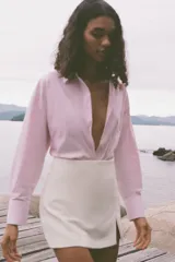 Camisa de popelín a rayas verticales rosas y blancas con hilo metalizado, de corte recto, cuello solapa, escote pico y manga larga.