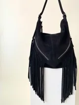 Bolso tipo hobo color tostado, hecho de cuero con flecos largos en el frente y dos bolsillos con cierre. Tiene una manija regulable con hebillas metálicas.