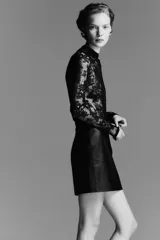 Pollera mini negra de tiro alto con acabado de efecto cuero. Presenta un corte recto y costura central en la espalda, con pinzas para estilizar la figura. La prenda está forrada.