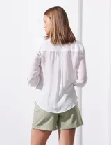 Blusa blanca de gasa marca Zac & Rachel, con cuello a la base, escote en V, abertura central con botones, bolsillo aplicado en el pecho y mangas largas regulables con presilla y botón. Tiene terminación opcional de nudo en el ruedo.