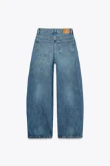 Jeans de tiro medio color azul denim, corte baggy, con trabillas y cinco bolsillos. Cierre frontal asimétrico con cremallera y botones metálicos.