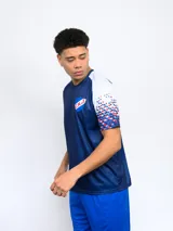 Remera deportiva azul con el escudo del Club Nacional de Football en el pecho y diseño de cuadros rojos y blancos en las mangas.