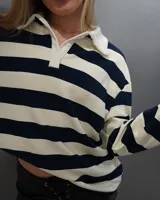 Remera polo manga larga a rayas horizontales azul marino y crema, con cuello blanco y tapeta de dos botones.