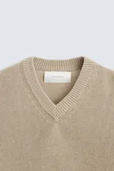 Jersey de punto color beige, con cuello en V y mangas largas.