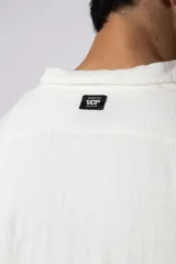 Camisa de lino blanca de manga larga, con cuello clásico y cierre frontal con botones. Corte recto y holgado.