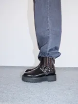 Botas de cuero color bordó con elástico en los laterales, detalle de bordado en hilo rojo en la puntera y hebillas con apliques metálicos. Plataforma de goma negra de 5 cm de altura.