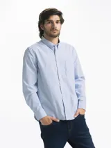 Camisa celeste y blanca a rayas verticales, de manga larga y corte clásico. Tiene cuello abotonado y bolsillo en el pecho.