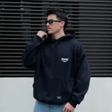 Canguro negro oversized con capucha y bolsillo delantero tipo canguro. Estampa pequeña en el pecho.