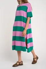 Vestido midi de tejido suave y ligero, con cuello redondo y mangas cortas. Presenta un patrón de rayas horizontales anchas en color verde oscuro y rosado. El vestido tiene aberturas laterales en el ruedo.