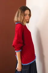 Sweater tejido rojo con cuello alto y puños con volados azules.