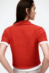 Cárdigan rojo de punto suave con cuello polo acanalado, cierre frontal con botones, mangas cortas y bolsillos delanteros decorativos con botón.