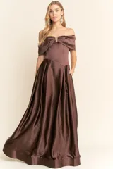 Vestido largo de fiesta color marrón chocolate, strapless con escote recto y detalle de abertura en el centro del busto. La falda es amplia y con pliegues, y tiene bolsillos laterales.