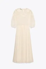 Vestido midi color crudo, con cuello redondo y mangas tres cuartos con elástico. Presenta combinación de tejidos y bordados a tono.