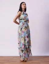 Vestido largo de gasa estampada con flores en tonos celeste, rosa y verde. Tiene cuello halter con abertura en forma de ojal, corte en la cintura con faja plisada y abertura central en la espalda con cierre invisible.