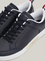 Zapatillas Tommy Hilfiger de cuero azul marino con suela blanca, cordones negros, interior blanco y detalles dorados en el talón y en el lateral.