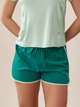 Short deportivo verde esmeralda con cintura elastizada con cordón ajustable y ribete blanco en ruedo y laterales.