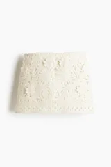 Minifalda entallada de tiro bajo, confeccionada en tejido bordado color crudo con apliques florales. Posee pinzas en la parte trasera y cierre oculto en un lateral.