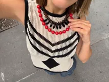 Chaleco calado negro con diseño de rayas diagonales rojas, beige y blancas.