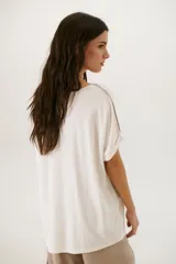 Remera negra de corte holgado con cuello redondo y mangas cortas con dobladillo. Presenta una línea diagonal blanca que cruza el frente desde el hombro hasta la cadera.
